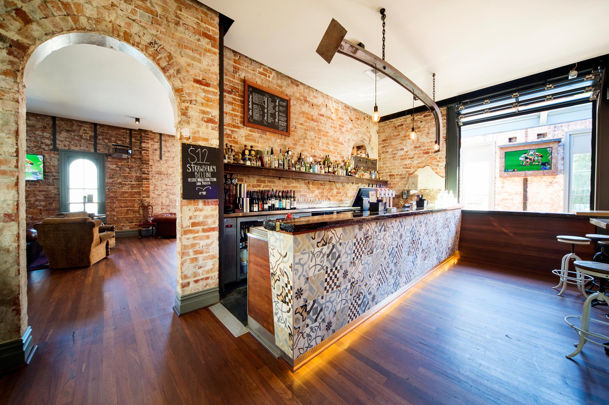 Upstairs bar at the Guildford Hotel with restored brick walls, coloured tiles on the bar, and suspended steel beam